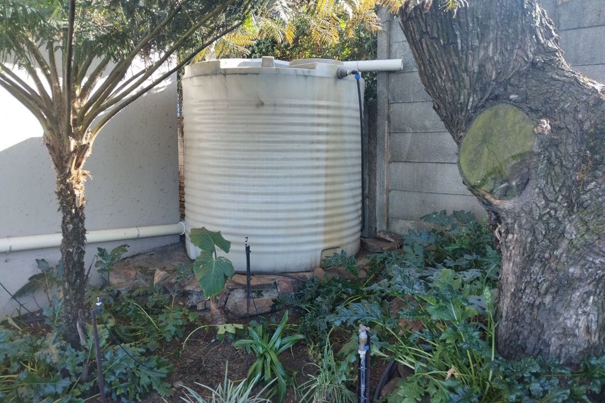 A rear garden area featuring a large water storage tank installed on a stone base against a concrete boundary wall.