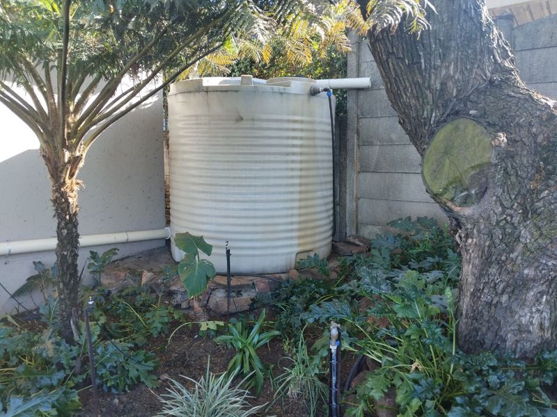 A rear garden area featuring a large water storage tank installed on a stone base against a concrete boundary wall.