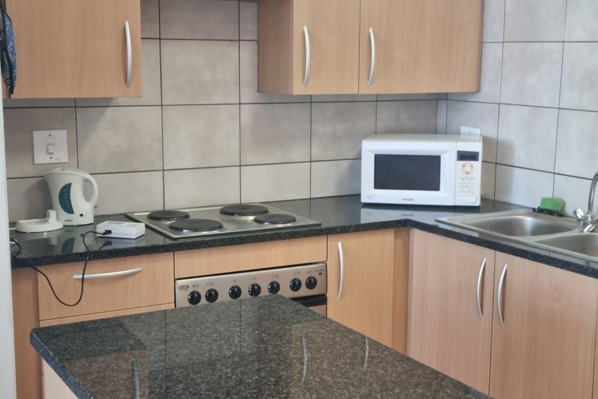 Functional kitchen featuring laminate cabinetry, granite countertops, tiled backsplash, and integrated electric hob and oven.