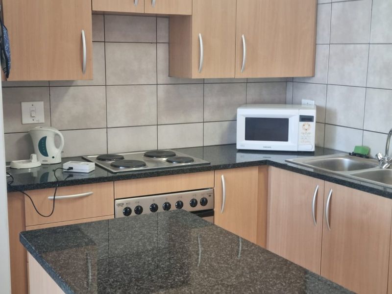 Functional kitchen featuring laminate cabinetry, granite countertops, tiled backsplash, and integrated electric hob and oven.