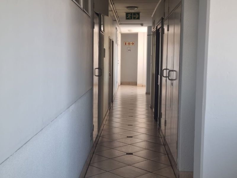 A functional apartment hallway featuring tiled flooring, built-in storage cupboards, and emergency exit signage.