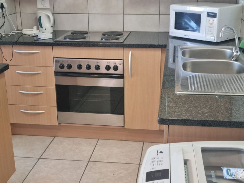 A functional kitchen featuring laminate cabinetry, granite countertops, a built-in oven with electric hob, and a double bowl stainless steel sink.