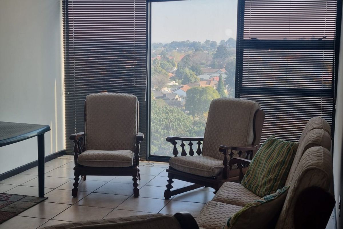 A bright living area featuring large floor-to-ceiling windows with venetian blinds, offering an expansive view and ceramic tile flooring throughout.