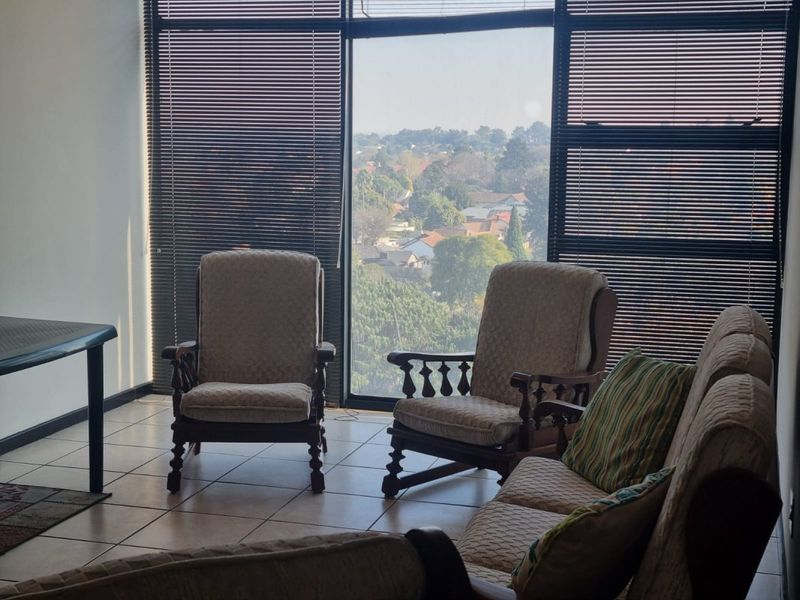 A bright living area featuring large floor-to-ceiling windows with venetian blinds, offering an expansive view and ceramic tile flooring throughout.