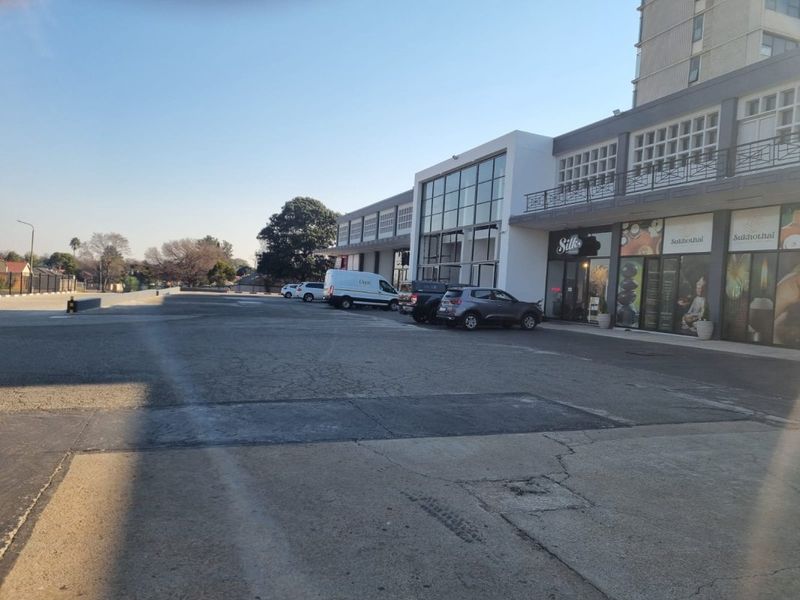 Exterior view of a commercial apartment building facade featuring ground-level storefronts, upper-level balconies, and an adjacent asphalt parking area.