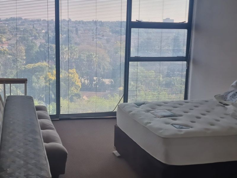 A bedroom featuring large floor-to-ceiling windows with venetian blinds, offering an elevated view of the surrounding landscape.