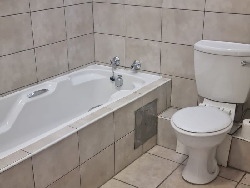 A functional bathroom featuring a built-in bathtub and toilet with neutral ceramic tiling, requiring minor repairs to the bathtub apron and finishes.