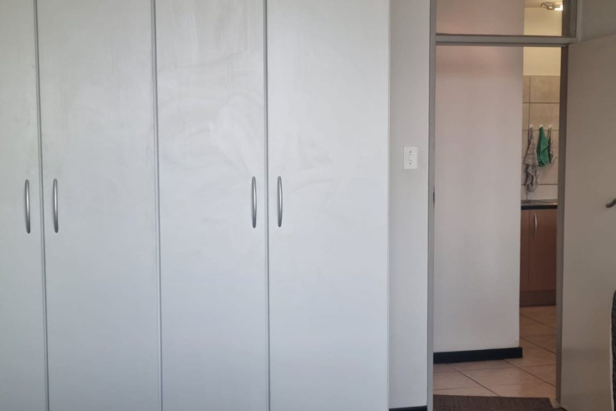 A bedroom featuring built-in cupboards with a view into an adjacent kitchen area.