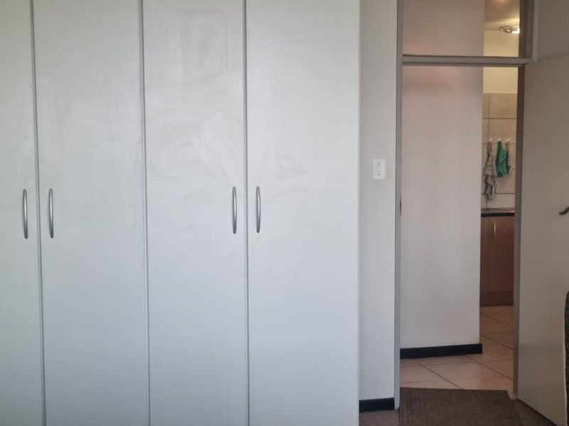 A bedroom featuring built-in cupboards with a view into an adjacent kitchen area.