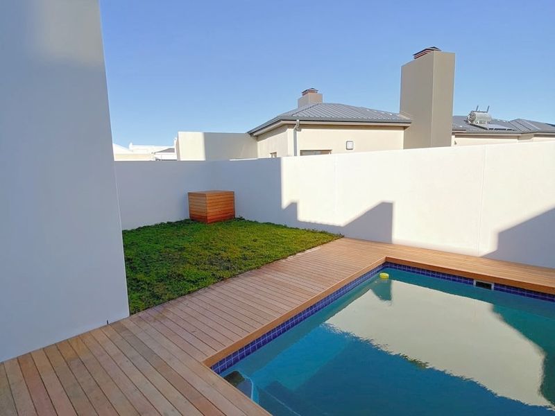 A private outdoor pool area featuring timber decking, a small lawn, and high boundary walls for privacy.
