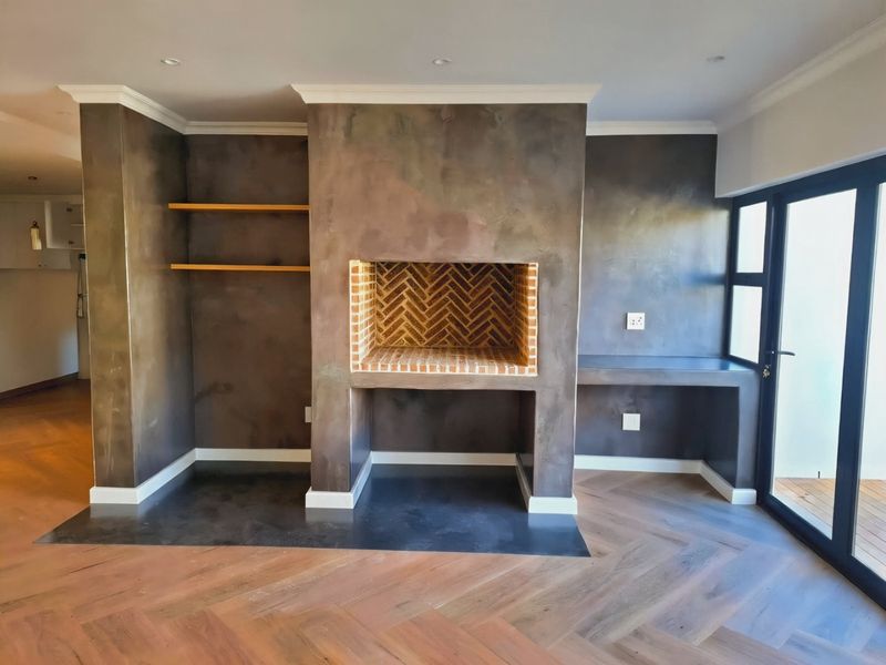 Spacious living area featuring a striking built-in fireplace with herringbone brick detail, custom shelving, a built-in desk, and elegant herringbone timber flooring.