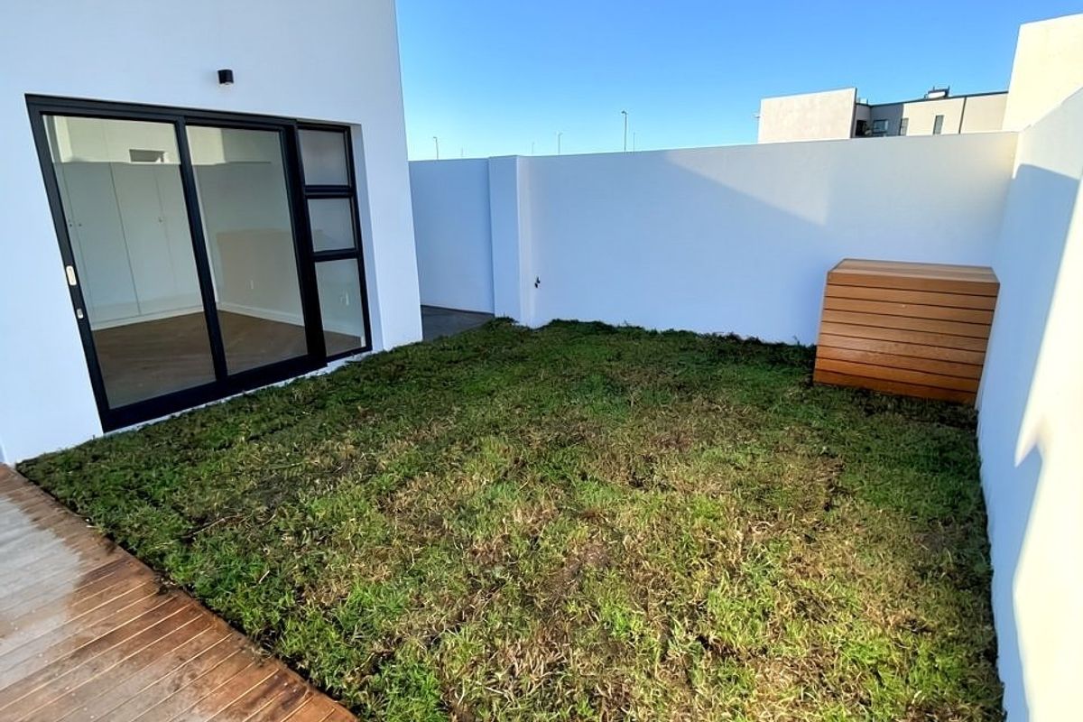 A private rear courtyard featuring timber decking, a small lawn area, and a modern sliding glass door providing access to the interior.