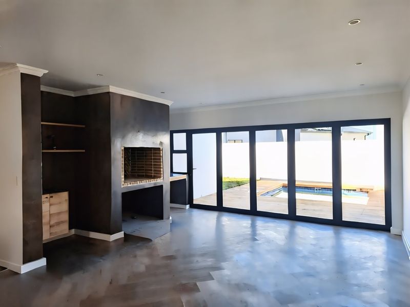 Spacious living area featuring a built-in fireplace, modern wooden flooring, and large bi-fold doors opening onto a deck with a swimming pool.