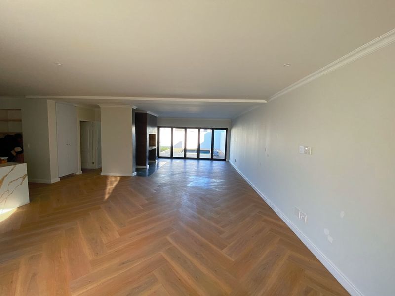 Spacious open-plan living area featuring herringbone timber flooring, a built-in fireplace, and large stacking glass doors leading to the outdoor area.