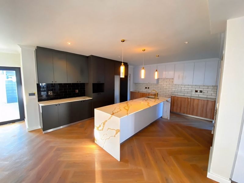 Modern kitchen featuring a large stone-topped island, herringbone timber flooring, contrasting dark and light cabinetry, and stylish pendant lighting.