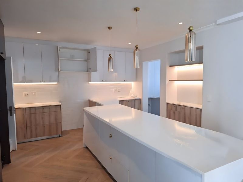 Modern kitchen featuring a large central island, sleek white and wood-tone cabinetry, stone countertops, and elegant pendant lighting with herringbone flooring.