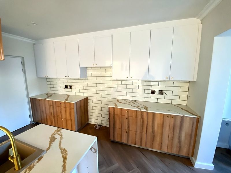 Modern kitchen featuring wood-grain cabinetry, marble-look quartz countertops, white subway tile backsplash, and herringbone wood flooring. Requires final electrical finishing.