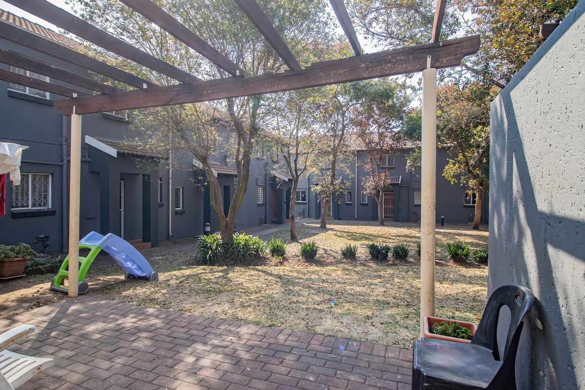 A rear view of the townhouse complex featuring a paved patio area with a timber pergola overlooking a shared garden space.