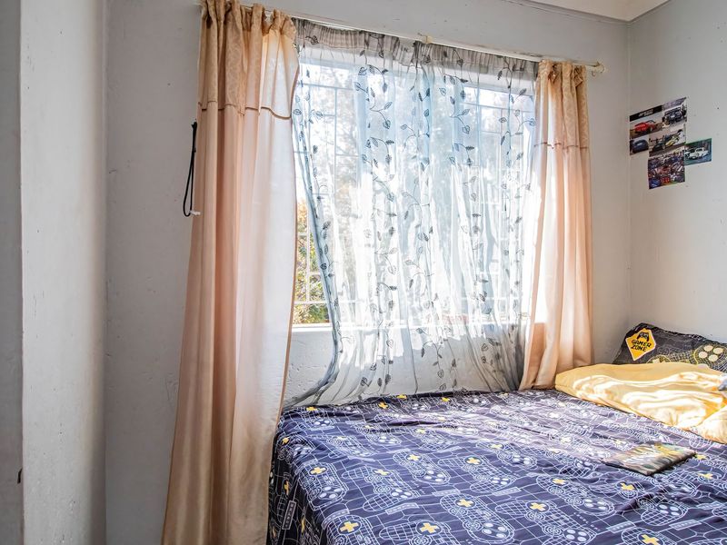 A bedroom featuring a window with security bars and curtain rod, showing signs of wear on the wall surfaces.