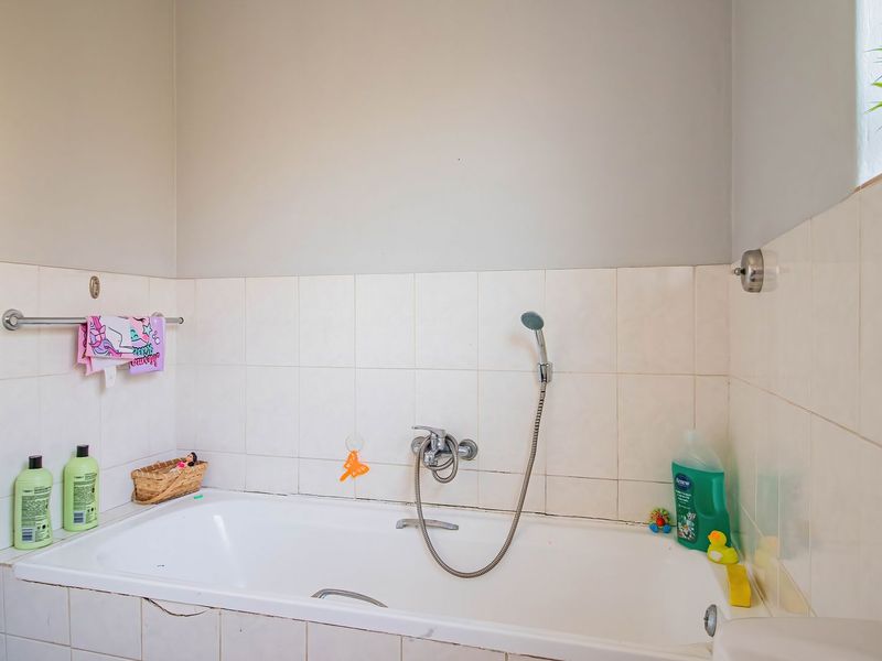 A functional bathroom featuring a built-in bathtub with a handheld shower mixer and tiled wall surrounds.