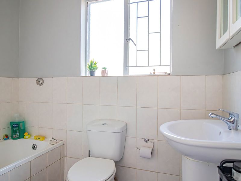 A functional bathroom featuring a pedestal basin, standard toilet, and a bathtub with a handheld shower attachment, finished with neutral wall tiling.