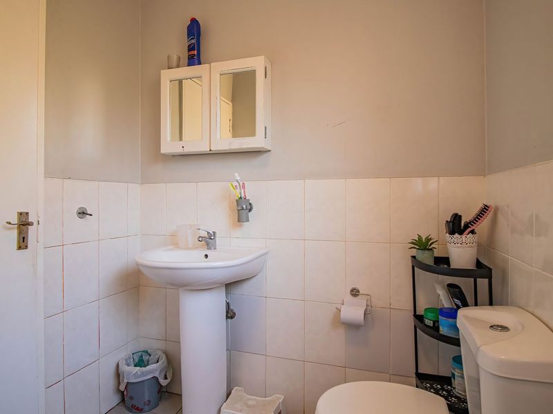 A compact bathroom featuring a pedestal basin, toilet, and wall-mounted medicine cabinet with tiled walls.