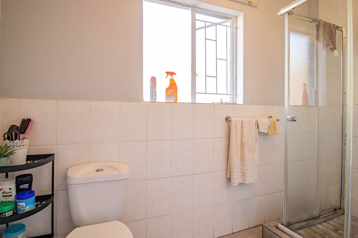 A functional bathroom featuring a shower enclosure, toilet, and tiled wall finishes, requiring some maintenance and cosmetic updates to improve its overall condition.
