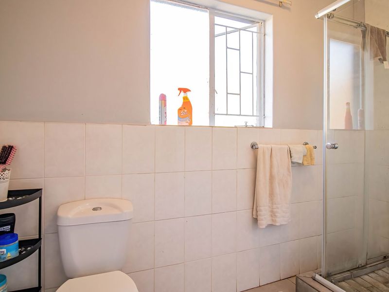 A functional bathroom featuring a shower enclosure, toilet, and tiled wall finishes, requiring some maintenance and cosmetic updates to improve its overall condition.