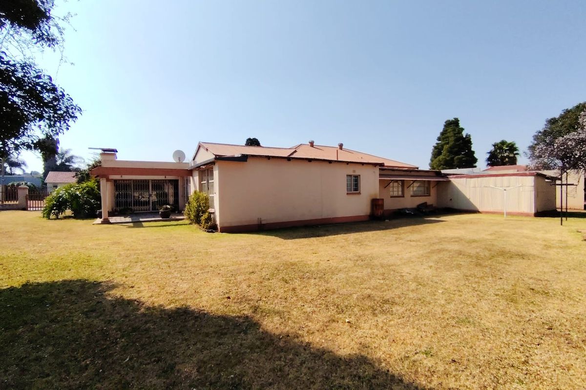 Rear view of the house featuring a large lawn, plastered masonry walls, a covered patio area, and a corrugated metal roof.