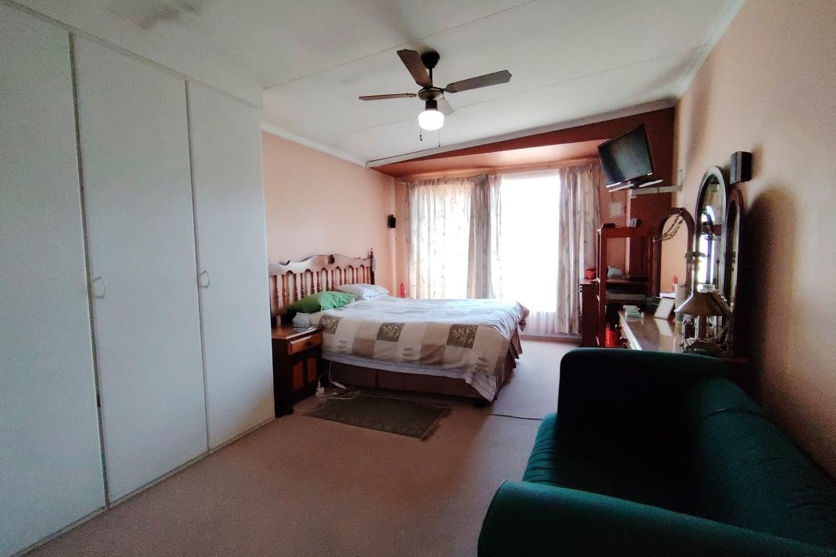 Spacious bedroom featuring built-in cupboards, a ceiling fan, and carpeted flooring, offering a functional layout with potential for modern updates.