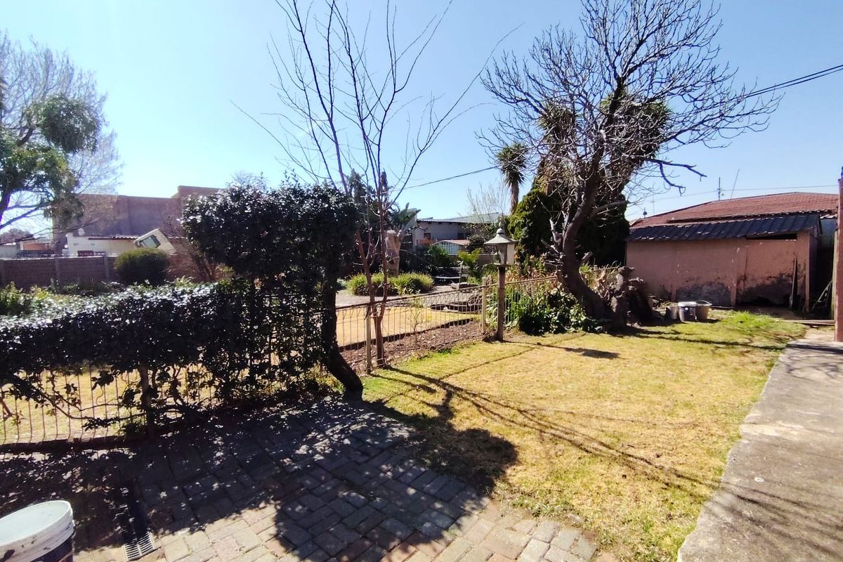 A rear garden area featuring a paved patio, lawn, wire fencing, and a detached outbuilding with visible exterior wear.