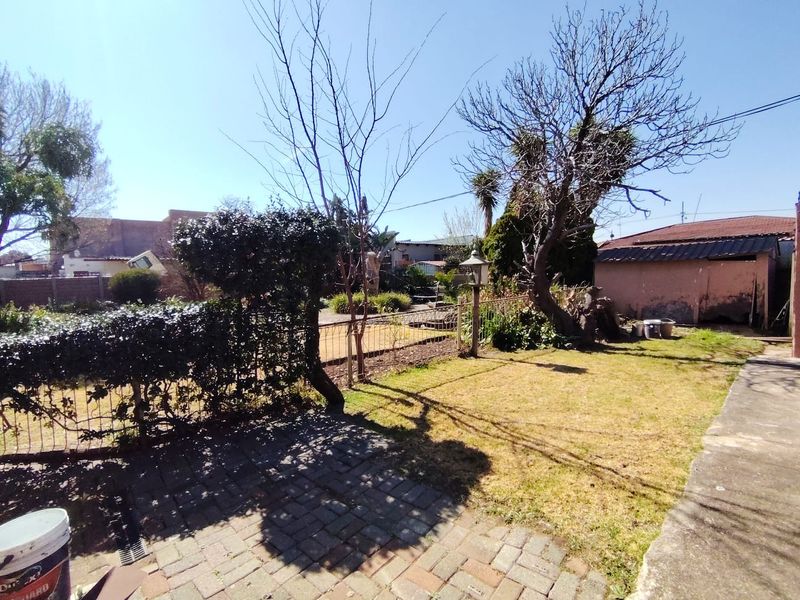 A rear garden area featuring a paved patio, lawn, wire fencing, and a detached outbuilding with visible exterior wear.