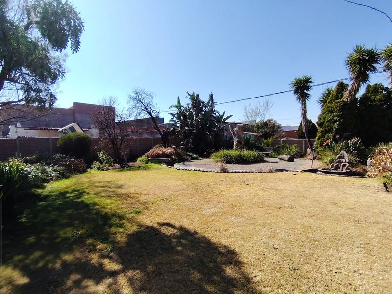 A spacious backyard garden featuring a central paved circular area, mature trees, and established landscaping enclosed by a brick boundary wall.