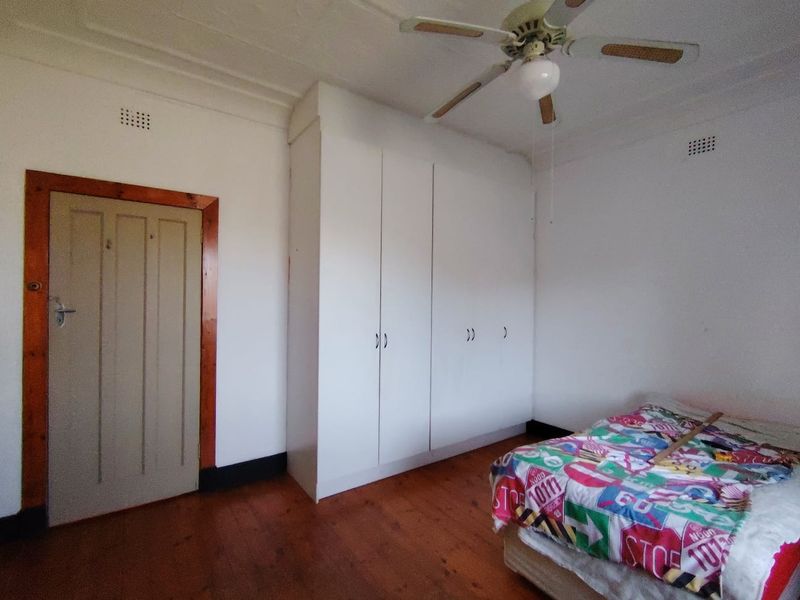 A bedroom featuring original timber flooring, a classic pressed metal ceiling, a ceiling fan, and built-in storage cupboards.