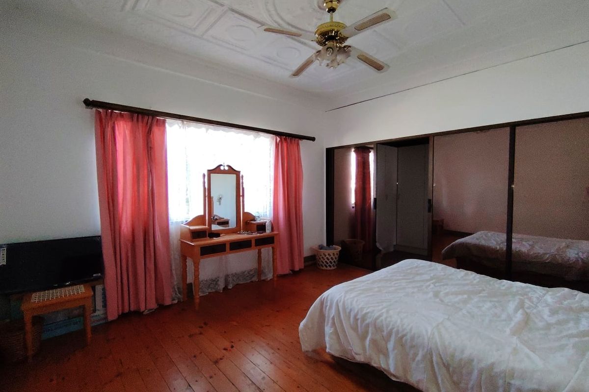 Spacious bedroom featuring polished timber flooring, an ornate ceiling rose with a central fan, and large built-in sliding door wardrobes.