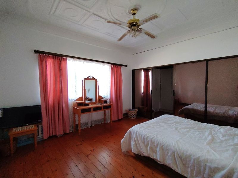 Spacious bedroom featuring polished timber flooring, an ornate ceiling rose with a central fan, and large built-in sliding door wardrobes.