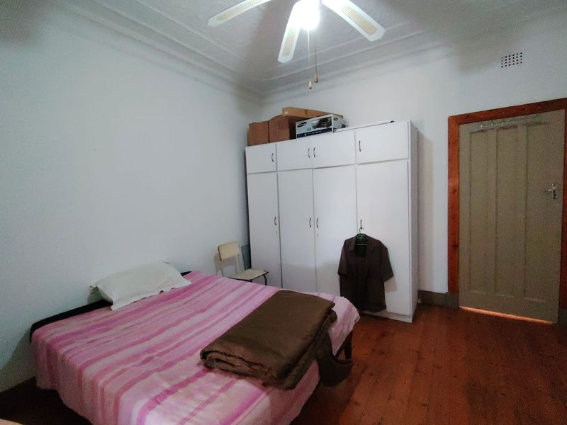 A bedroom featuring original timber flooring, ornate ceiling cornices, a ceiling fan, and a large built-in wardrobe for storage.