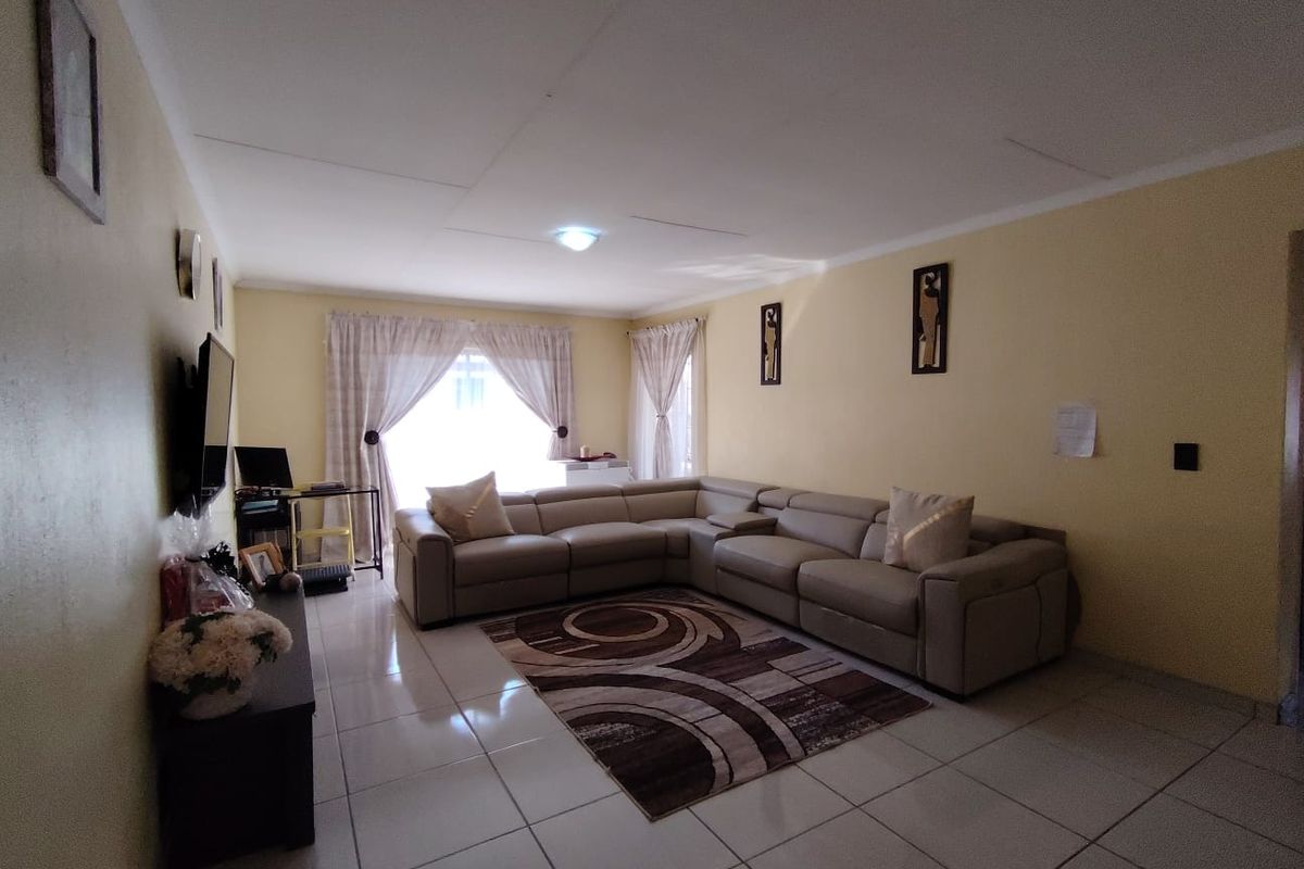 A spacious living room featuring neutral tiled flooring, soft wall tones, and a large sliding glass door providing natural light.