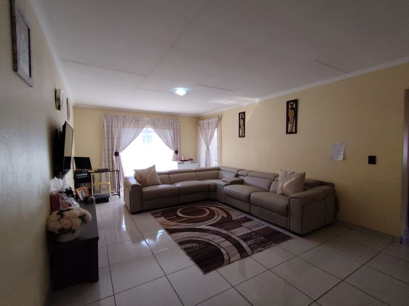 A spacious living room featuring neutral tiled flooring, soft wall tones, and a large sliding glass door providing natural light.