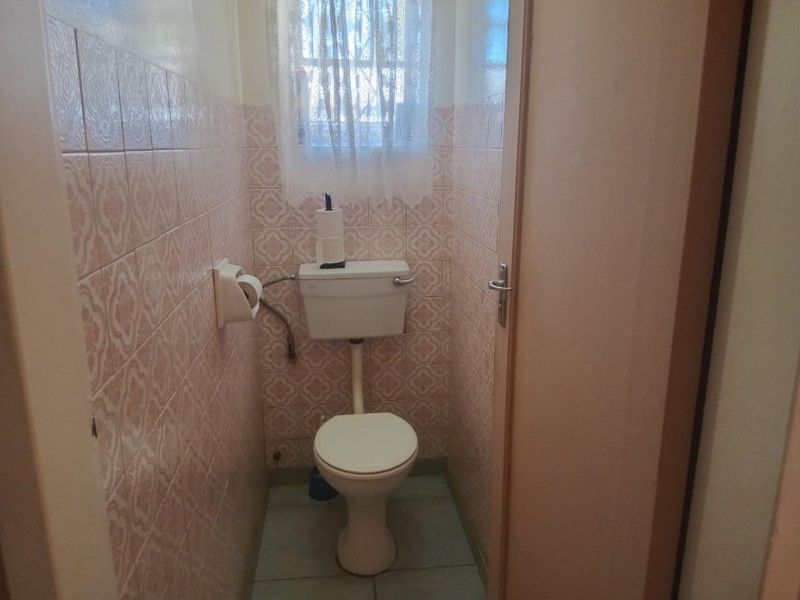A compact, dated guest toilet featuring original patterned wall tiles and standard ceramic fixtures.
