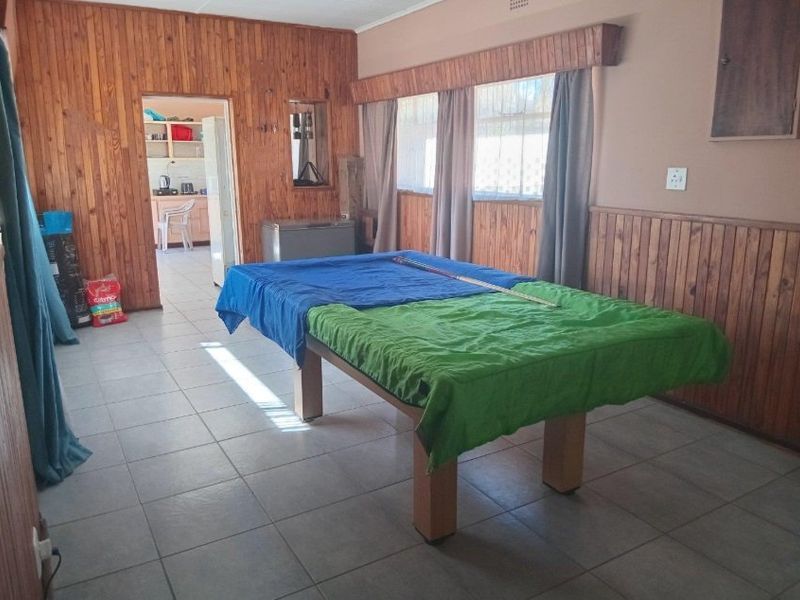 Living area featuring timber wall paneling, tiled flooring, and window pelmets, with an adjacent view into the kitchen area.