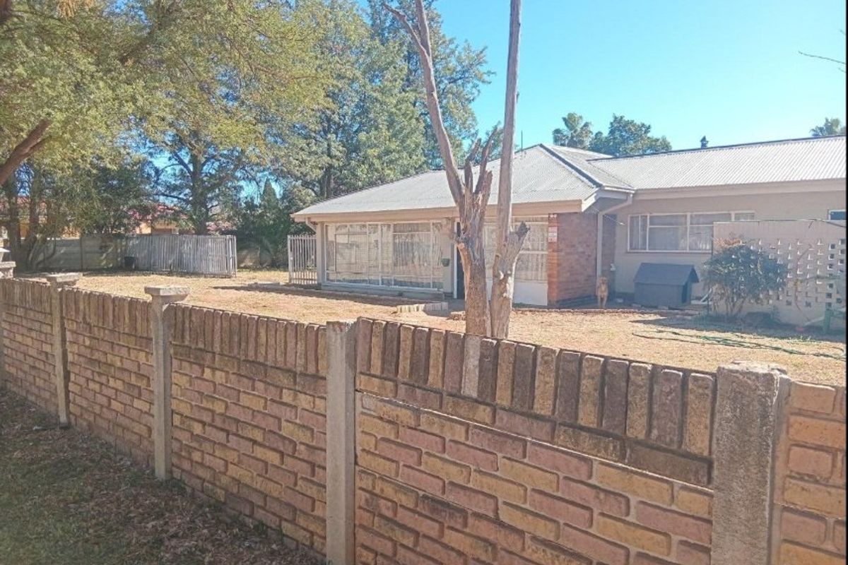 Rear view of the property featuring a brick boundary wall, corrugated metal roof, and an enclosed patio area set within a spacious garden.