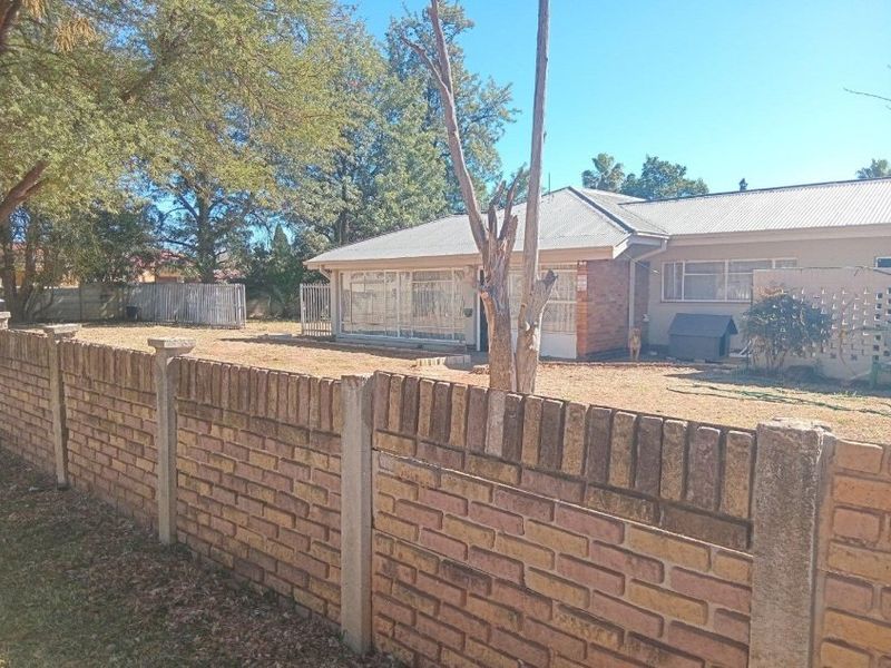 Rear view of the property featuring a brick boundary wall, corrugated metal roof, and an enclosed patio area set within a spacious garden.