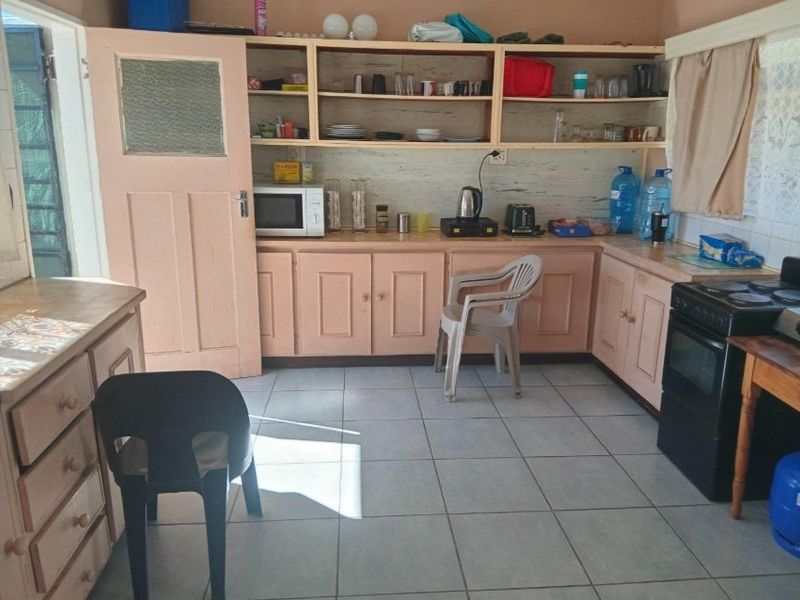 A functional kitchen featuring tiled flooring, built-in cabinetry with open shelving, and a freestanding oven, offering potential for cosmetic updates.