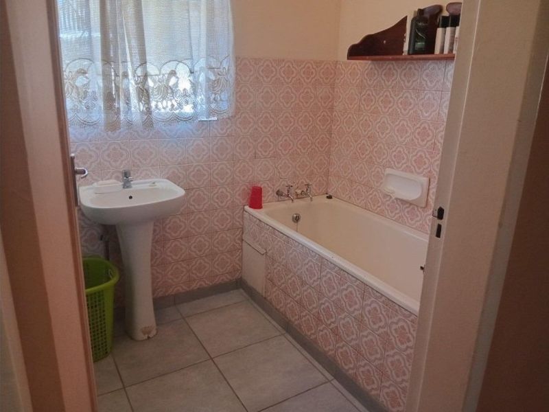 A functional bathroom featuring a pedestal basin and a built-in bathtub with dated patterned wall tiling.
