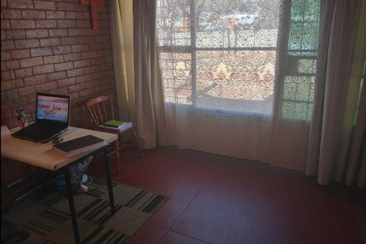 A bedroom featuring an exposed brick wall, tiled flooring, and a large window with security bars.