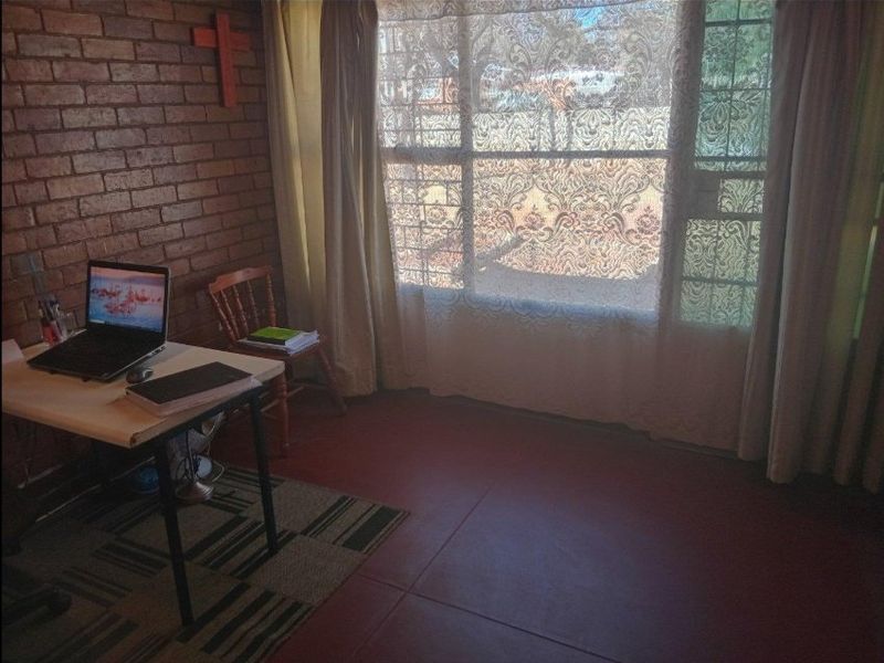 A bedroom featuring an exposed brick wall, tiled flooring, and a large window with security bars.