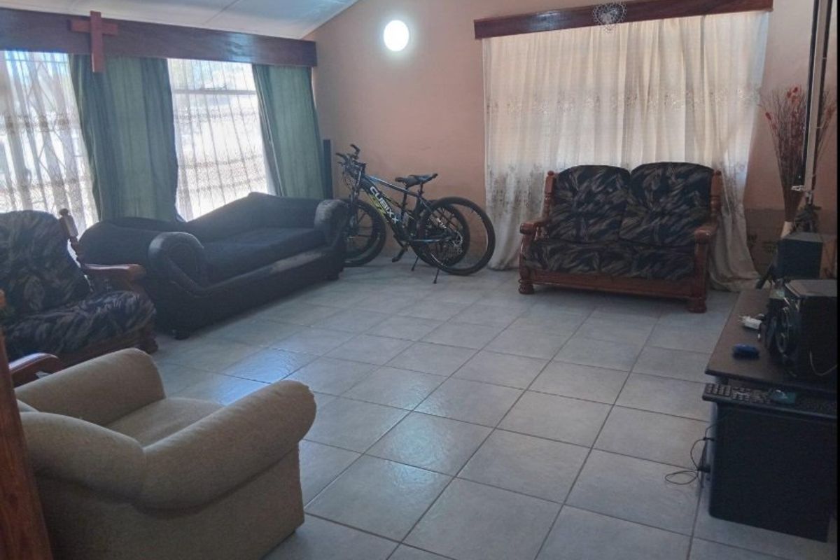 Spacious living room featuring tiled flooring, vaulted ceilings, and large windows with timber pelmets, offering a functional and well-lit living space.