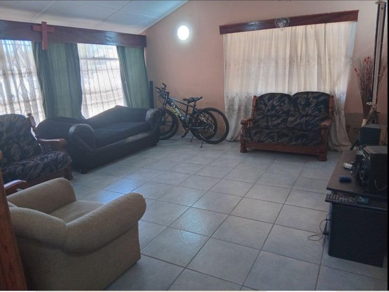 Spacious living room featuring tiled flooring, vaulted ceilings, and large windows with timber pelmets, offering a functional and well-lit living space.