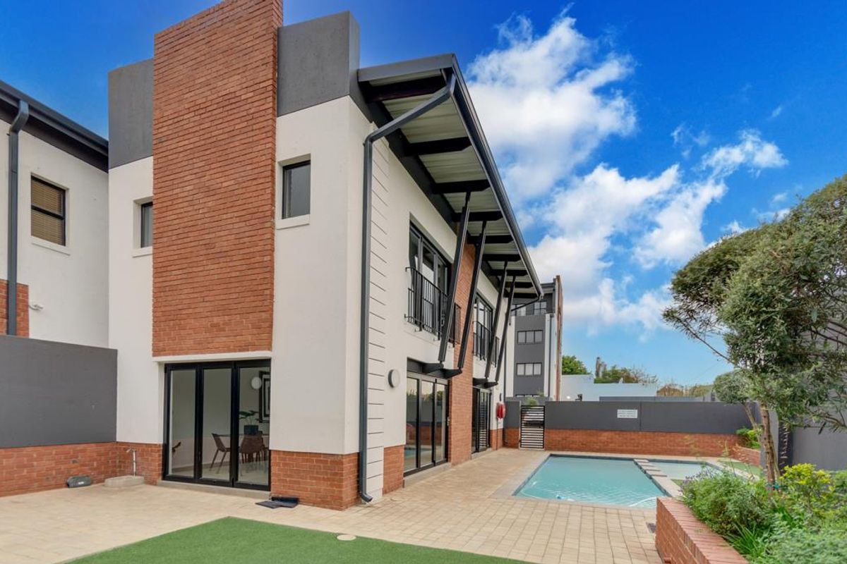 Rear view of a modern apartment building featuring a private swimming pool, paved patio area, and contemporary brick and render facade.